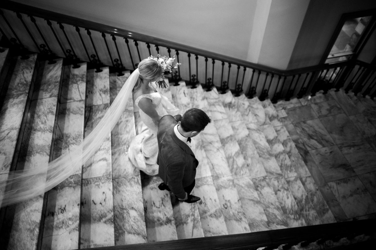 Black and white photo. Aerial view of a bride and groom descending the marble stairs at Adelaide Town Hall.